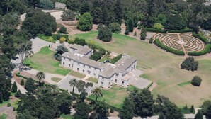 An aerial view of a large, historic building with a symmetrical facade, surrounded by well-maintained gardens and a formal lawn.