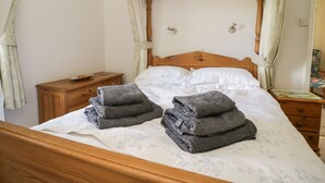 Un dormitorio con una cama con dosel de madera, una mesita de noche, una silla y un aparador de madera.