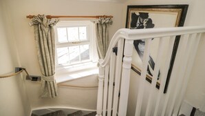 Una escalera con barandas blancas, una ventana con cortinas y un cuadro en la pared.