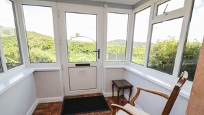 Habitación iluminada por el sol con vistas a colinas verdes, una puerta con una placa, una silla de madera y una pequeña mesa.