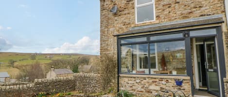 A stone building with a modern glass extension, a stone wall, and a view of the countryside.