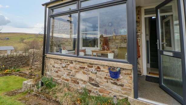 A stone house with a large glass window and door, a small outdoor seating area, and a view of the countryside. - 1 Braeside (Bishop Auckland)