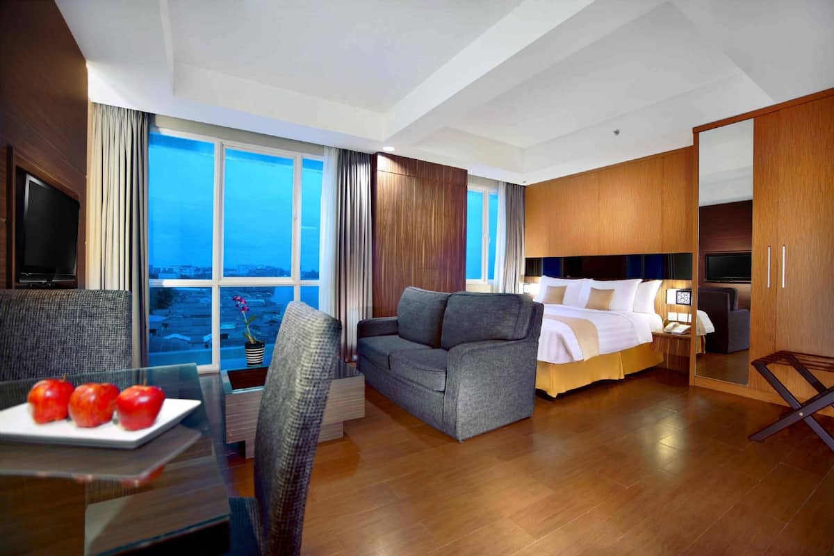 Ein Hotelzimmer mit einem großen Bett, einem Sofa, einem Fernseher und einem Essbereich mit Äpfeln auf einem Tisch.
