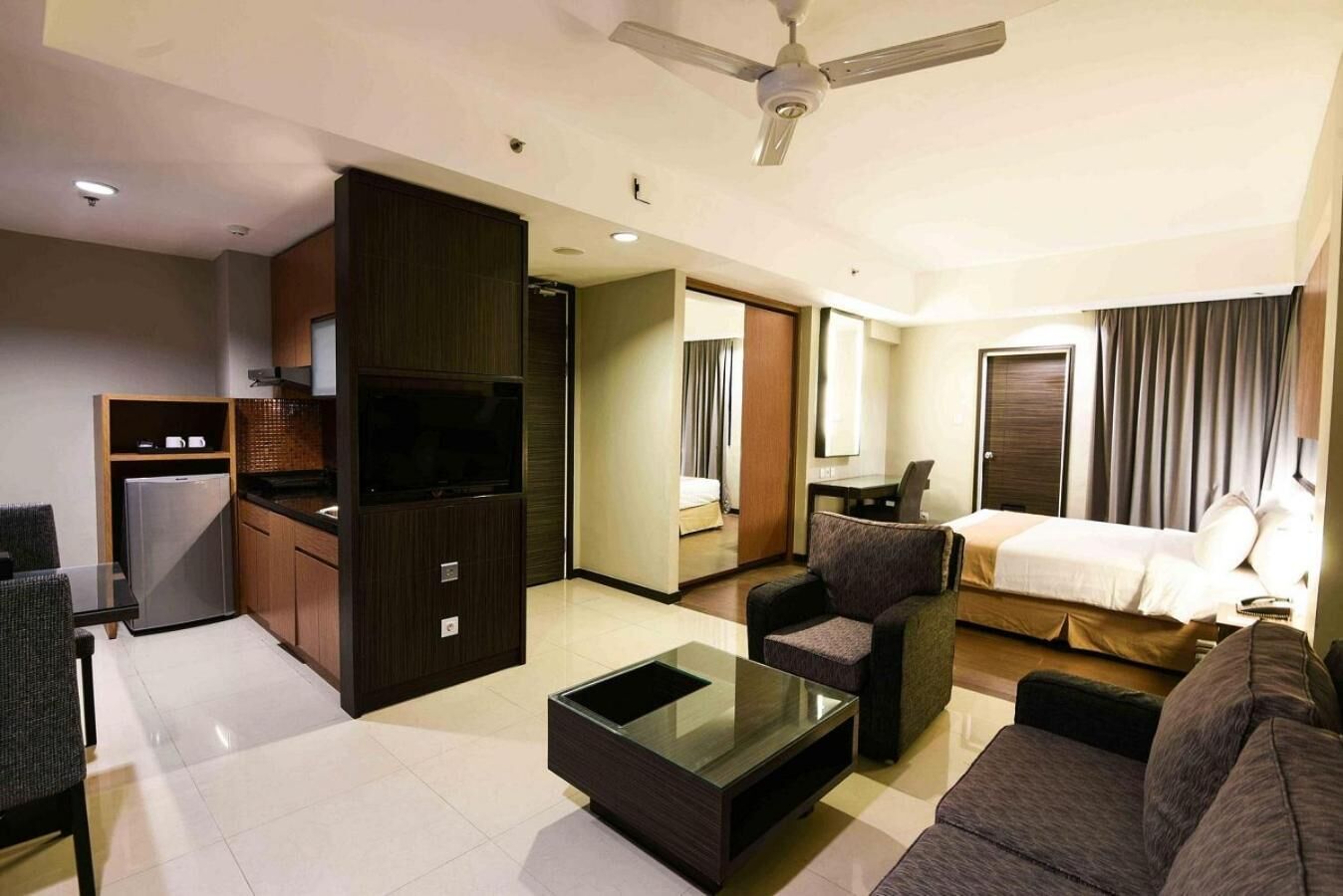 A modern hotel room with a kitchenette, a flat-screen TV, a sofa, a coffee table, and a bed.