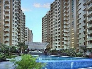 A high-rise residential building with multiple balconies, a swimming pool, and surrounding greenery. - The Malibu Suites Balikpapan by Sissae Living (Balikpapan)