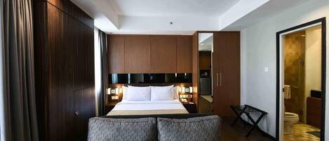 A hotel room with a bed, bedside tables, a sofa, a wardrobe, and a bathroom visible through an open door.