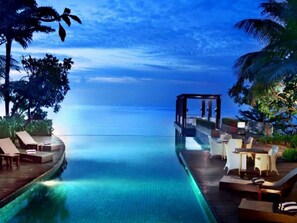 An infinity pool with a wooden deck, lounge chairs, and a small structure with a glass top. - The Malibu Suites Balikpapan by Sissae Living (Balikpapan)