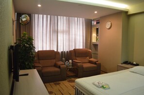 A hotel room with two brown armchairs, a small table, a bed, a nightstand, a clock, and a mirror. - Rivan Hotel Longgang Shenzhen (Shenzhen)