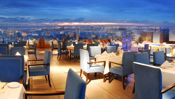 A rooftop restaurant with tables set for dining, overlooking a cityscape at dusk. - Rivan Hotel Longgang Shenzhen (Shenzhen)