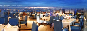A rooftop restaurant with tables set for dining, overlooking a cityscape at dusk. - Rivan Hotel Longgang Shenzhen (Shenzhen)