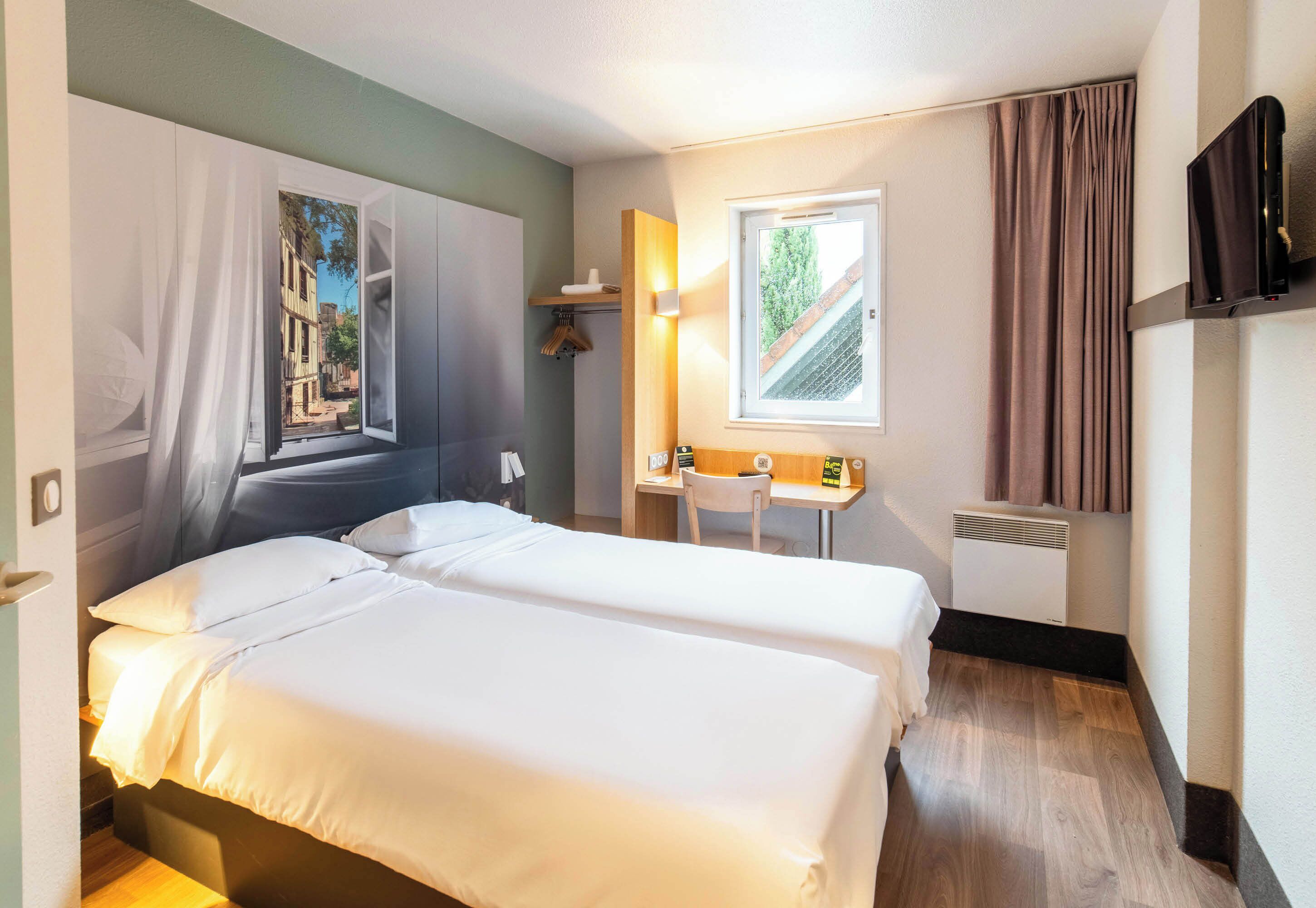 A hotel room with two beds, a desk, a chair, a TV, and a window with curtains.