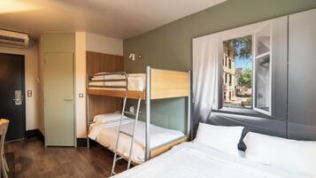 Habitación de hotel con literas, un escritorio y ventana con vista a edificios.