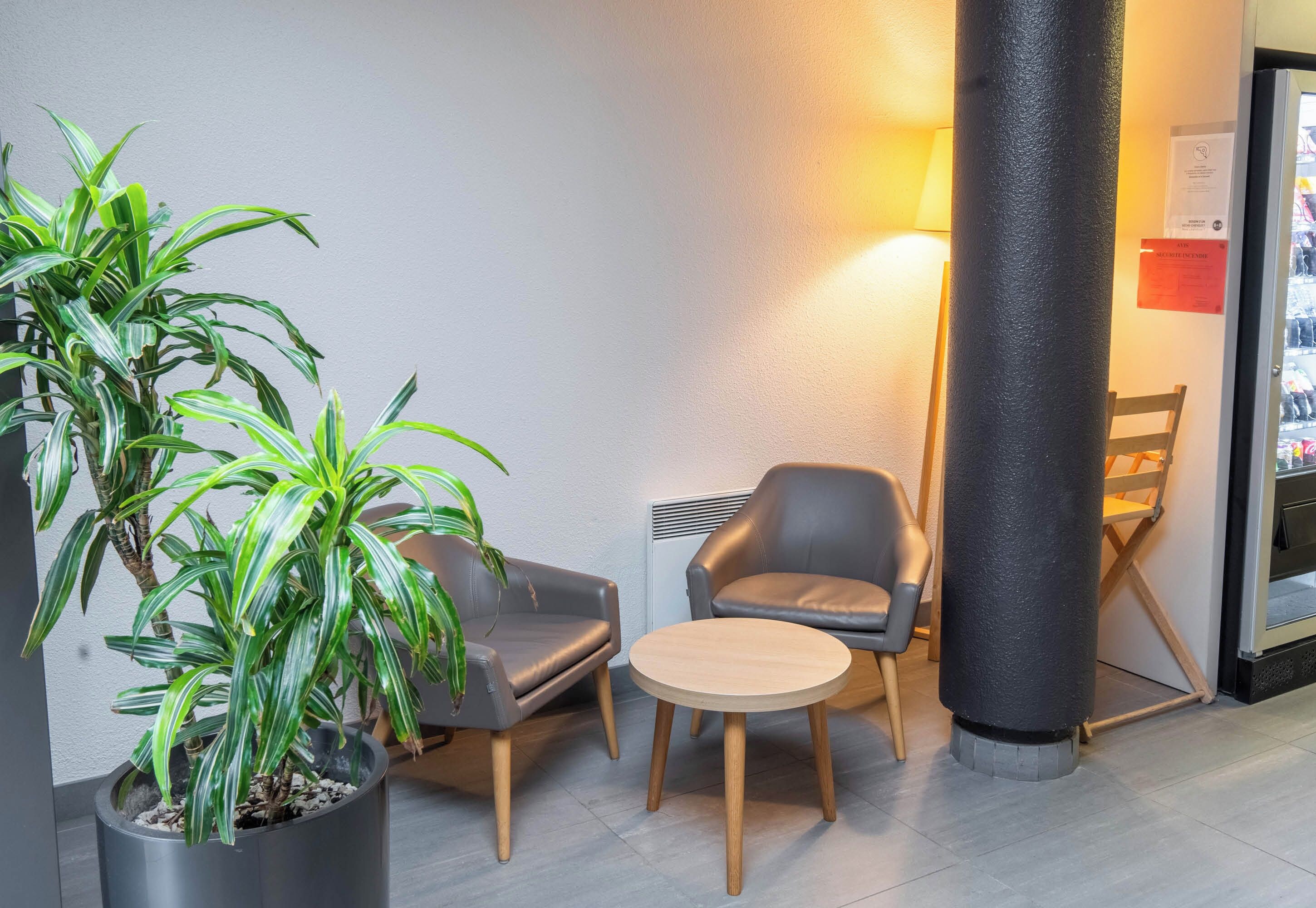 Un vestíbulo moderno con una planta en maceta, dos sillones de cuero, una mesa redonda de madera y un pilar grande.