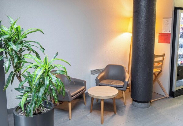 Un hall d’entrée moderne agrémenté d’une plante en pot, de deux fauteuils en cuir, d’une table ronde en bois et d’un grand pilier.