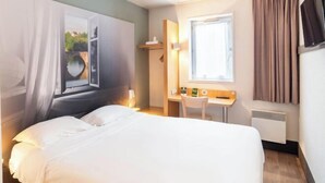 Ein Hotelzimmer mit Bett, Schreibtisch, Stuhl, Fenster und Fernseher.