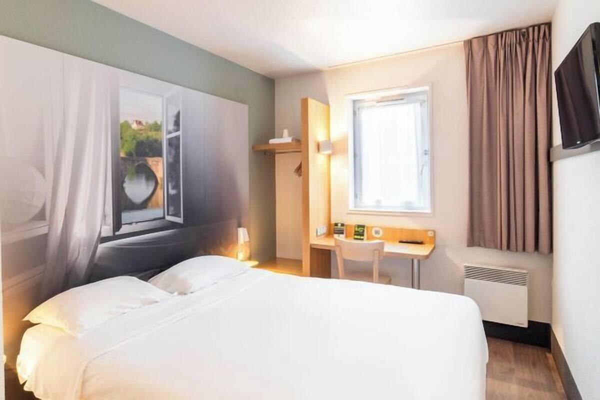 Une chambre d’hôtel avec un lit, un bureau, une chaise, une fenêtre et un téléviseur.
