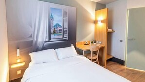 Ein Hotelzimmer mit Bett, Schreibtisch und einem an der Wand befestigten Fernseher.