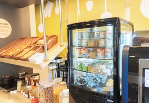 A refrigerated display case with various food items and a counter with baskets and condiments. - B&B Hotel Limoges 1 (Limoges)