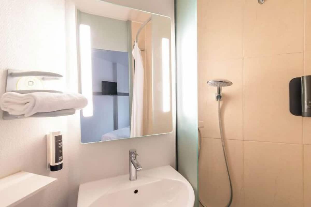 Une salle de bain moderne avec un lavabo blanc, un miroir, un porte-serviettes et une douchette à main.