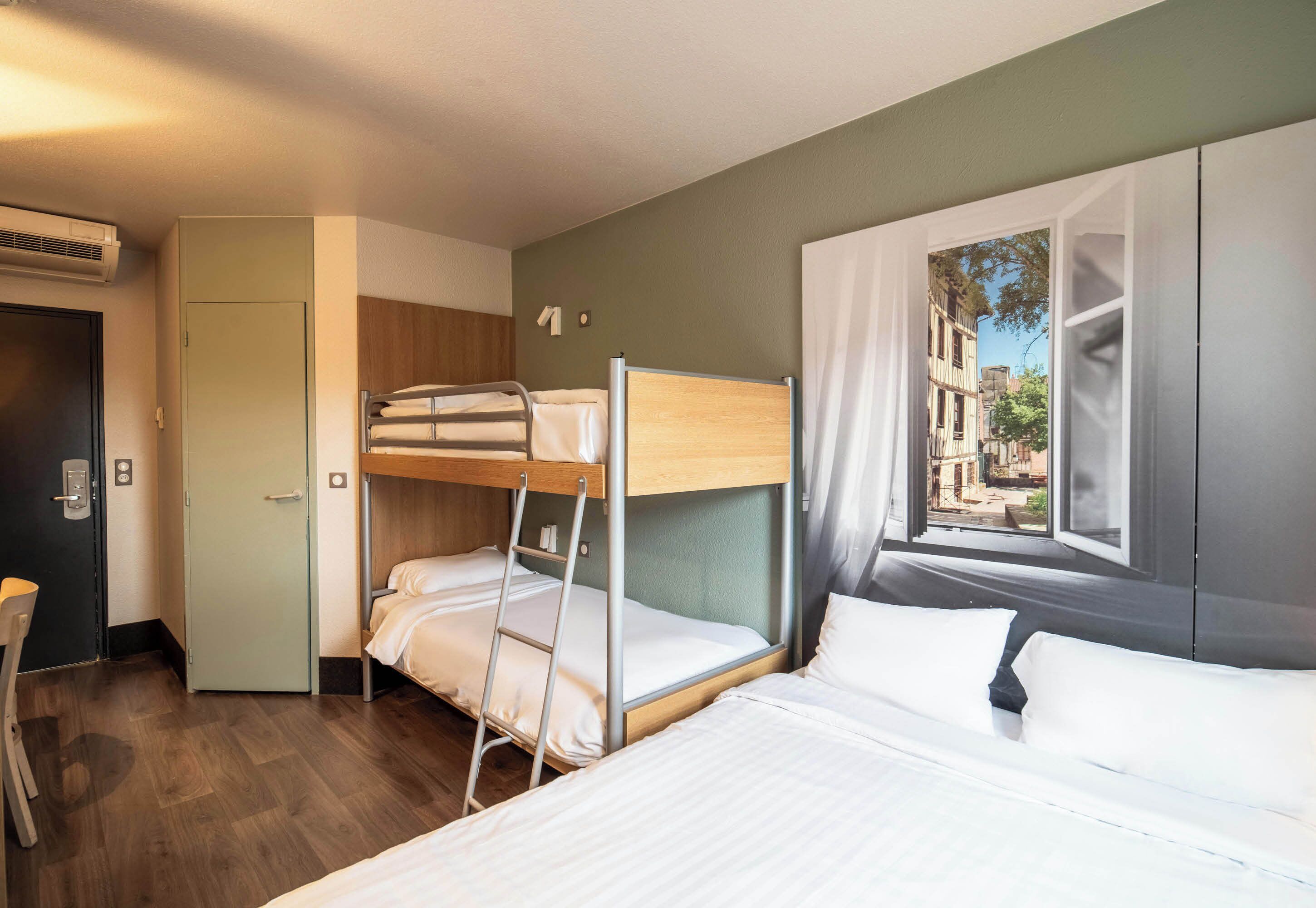 A hotel room with bunk beds, a desk, and a window with a view of buildings.