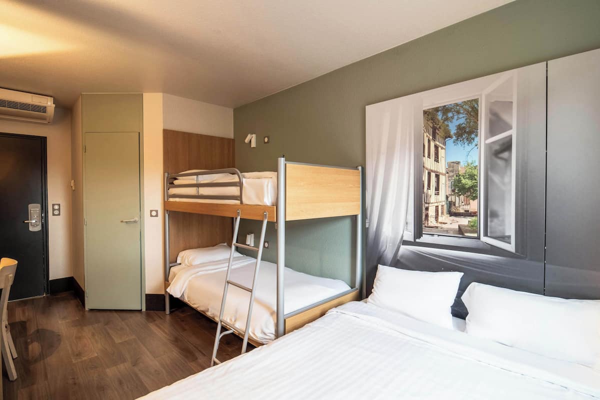 Une chambre d’hôtel avec des lits superposés, un bureau et une fenêtre donnant sur des immeubles.
