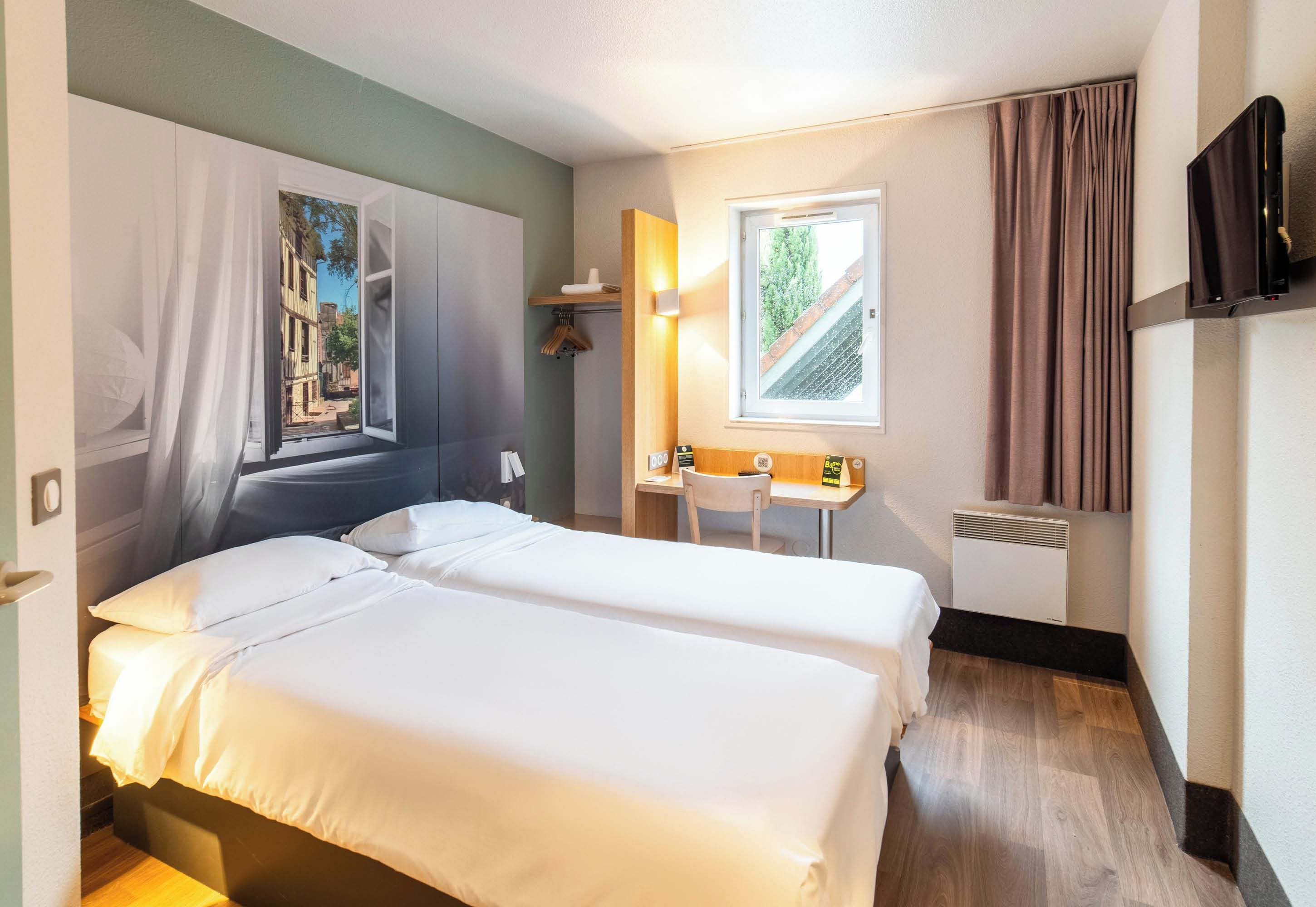 Hotelkamer met twee bedden, een bureau, een stoel, een televisie en een raam met gordijnen.
