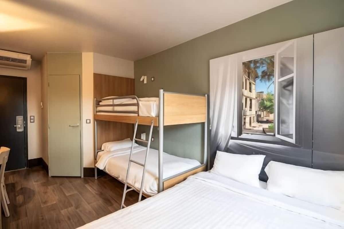 Une chambre d’hôtel avec un lit superposé, un bureau et une fenêtre avec des rideaux.