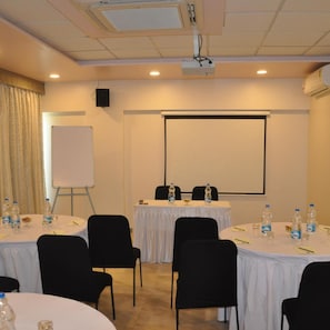 A conference room with tables, chairs, a projector screen, and a whiteboard. - Hotel Green Olive (AURANGABAD)