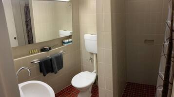 A bathroom with a white sink, a toilet, and a mirror above the sink. There is a towel hanging on the wall and a shower curtain.