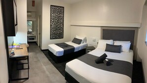 Habitación de hotel con dos camas, un escritorio, un televisor y un panel decorativo en la pared.