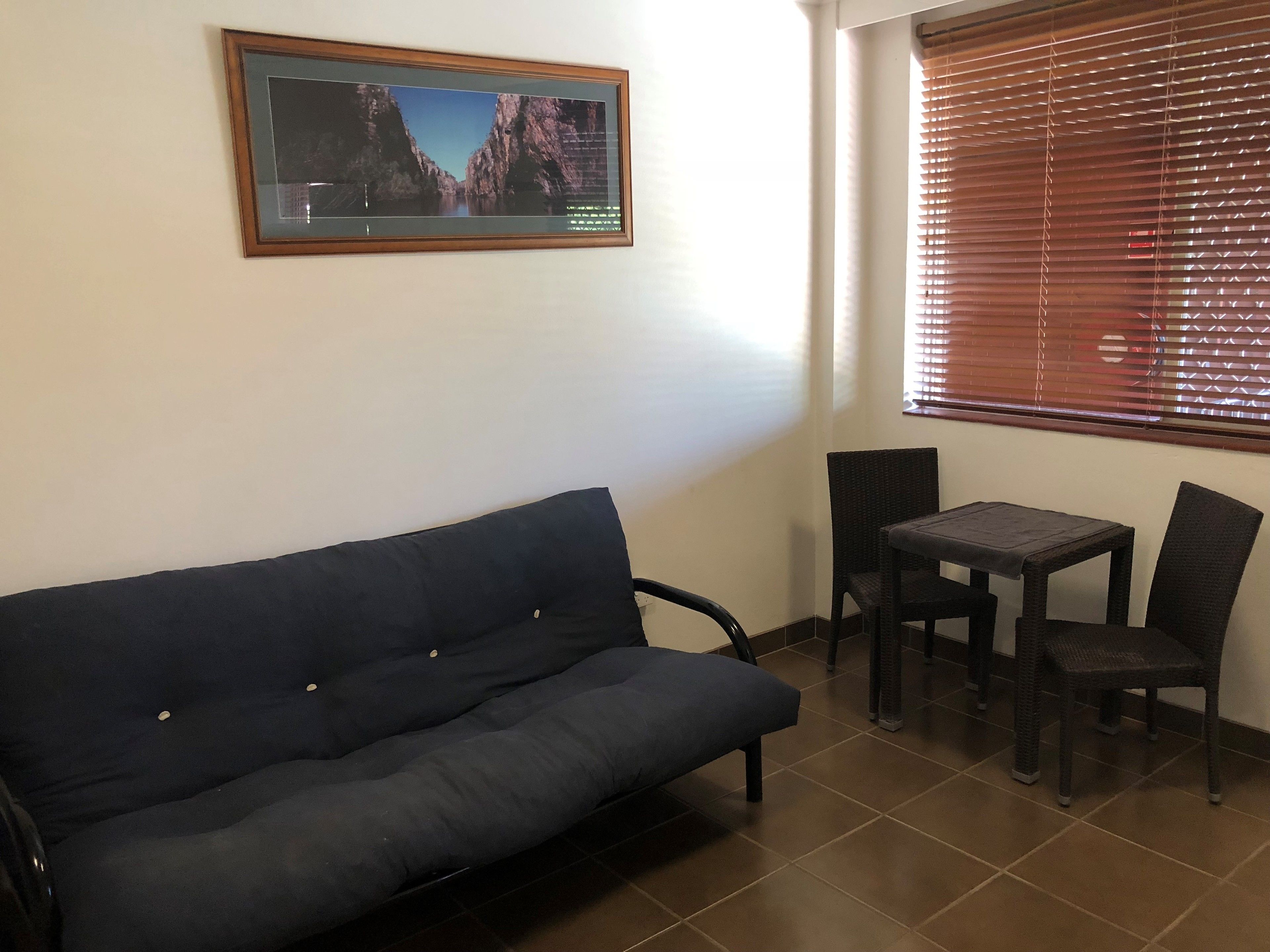 A room with a dark blue sofa, a small table with two chairs, and a framed picture on the wall.
