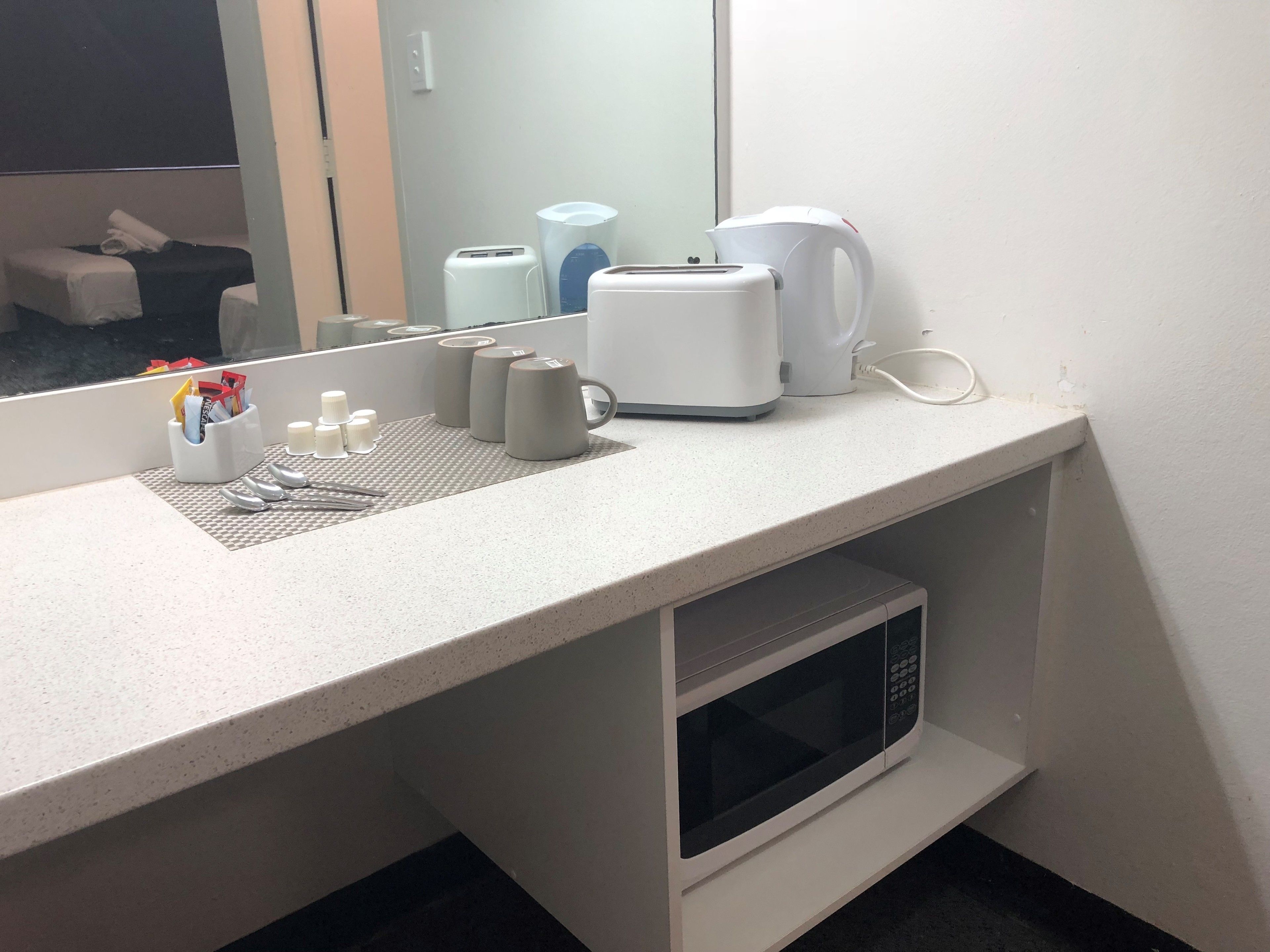 Un baño de hotel con encimera, microondas, hervidor y espejo.