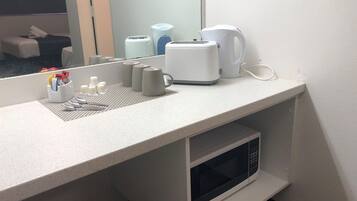Un baño de hotel con encimera, microondas, hervidor y espejo.