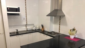 Una cocina con armarios blancos, encimera negra, microondas, tostadora y campana extractora de acero inoxidable.