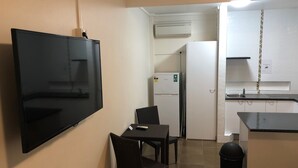 Una cocina compacta con un televisor de pantalla plana montado en la pared, un refrigerador y un pequeño comedor con mesa y sillas.