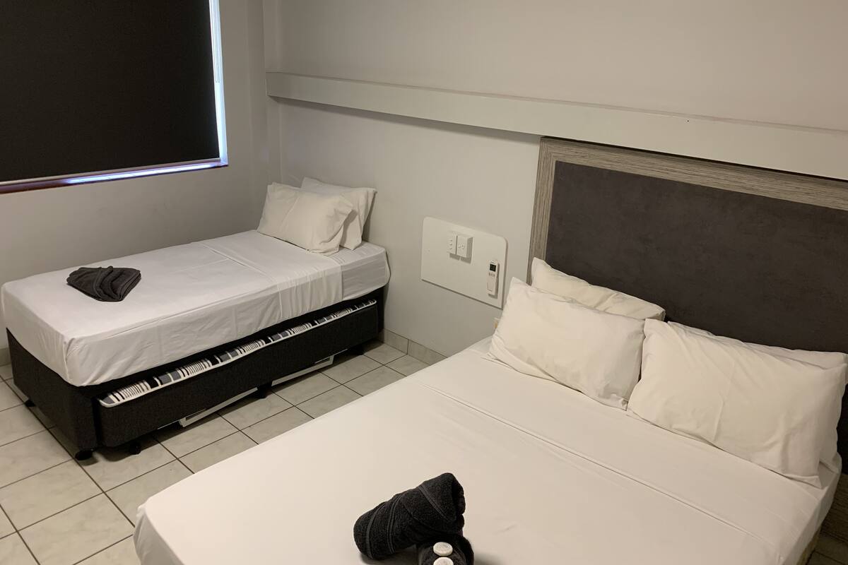A hotel room with two beds, a piano, a control panel, and a window.