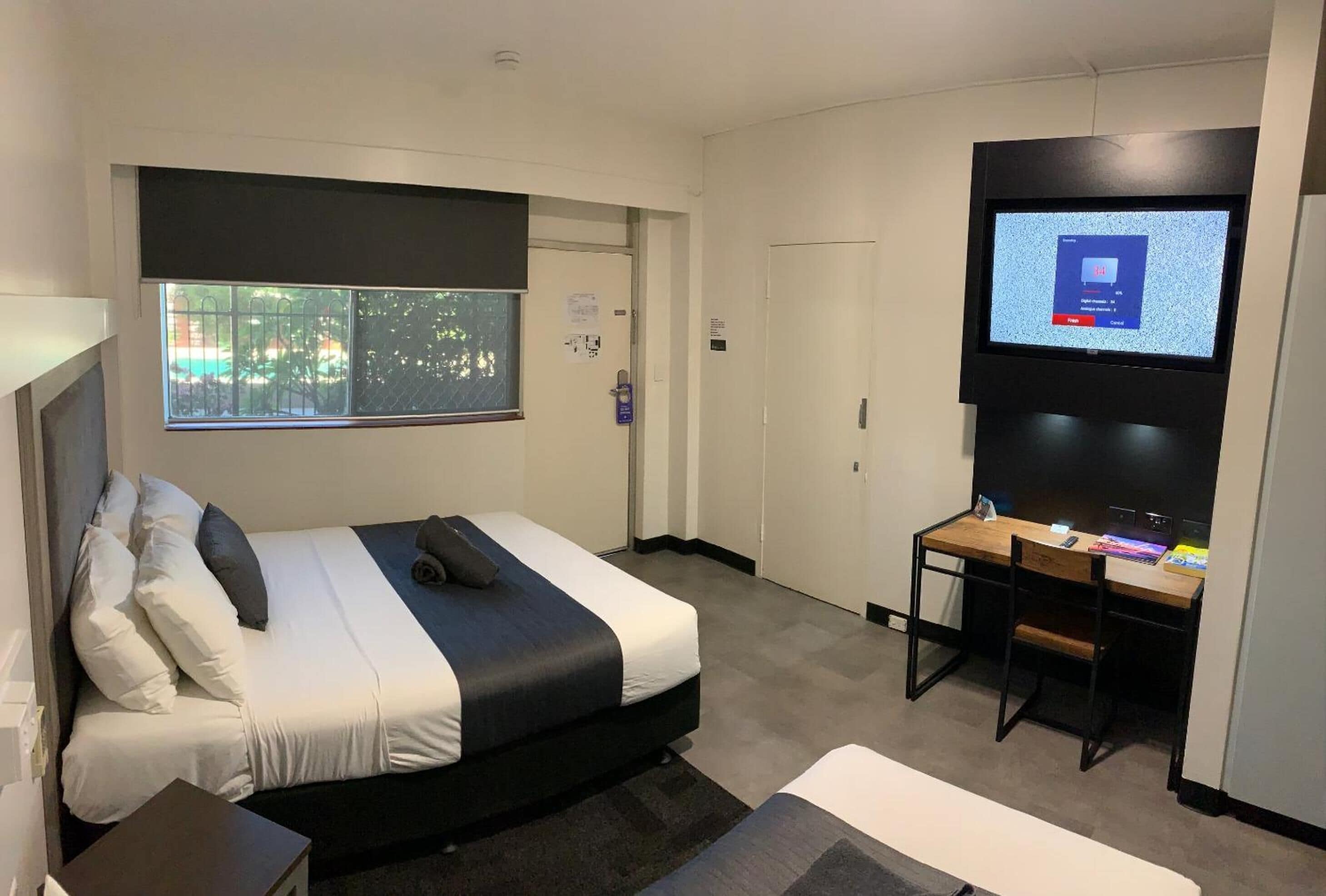 A modern hotel room with a bed, a desk, a television, and a window with a view of trees.