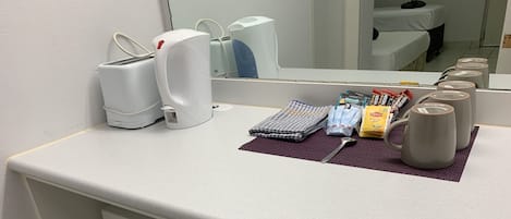 Habitación de hotel con encimera blanca, microondas, cafetera, hervidor de agua, libreta y cuchara.
