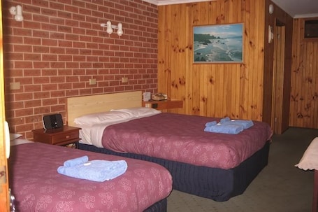 A room with two beds, wooden walls, a painting, and a small table with a lamp.. Orbost Country Road Motor Inn