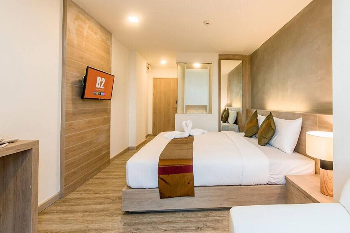 Habitación de hotel con cama, escritorio, televisor, espejo y lámpara de noche.