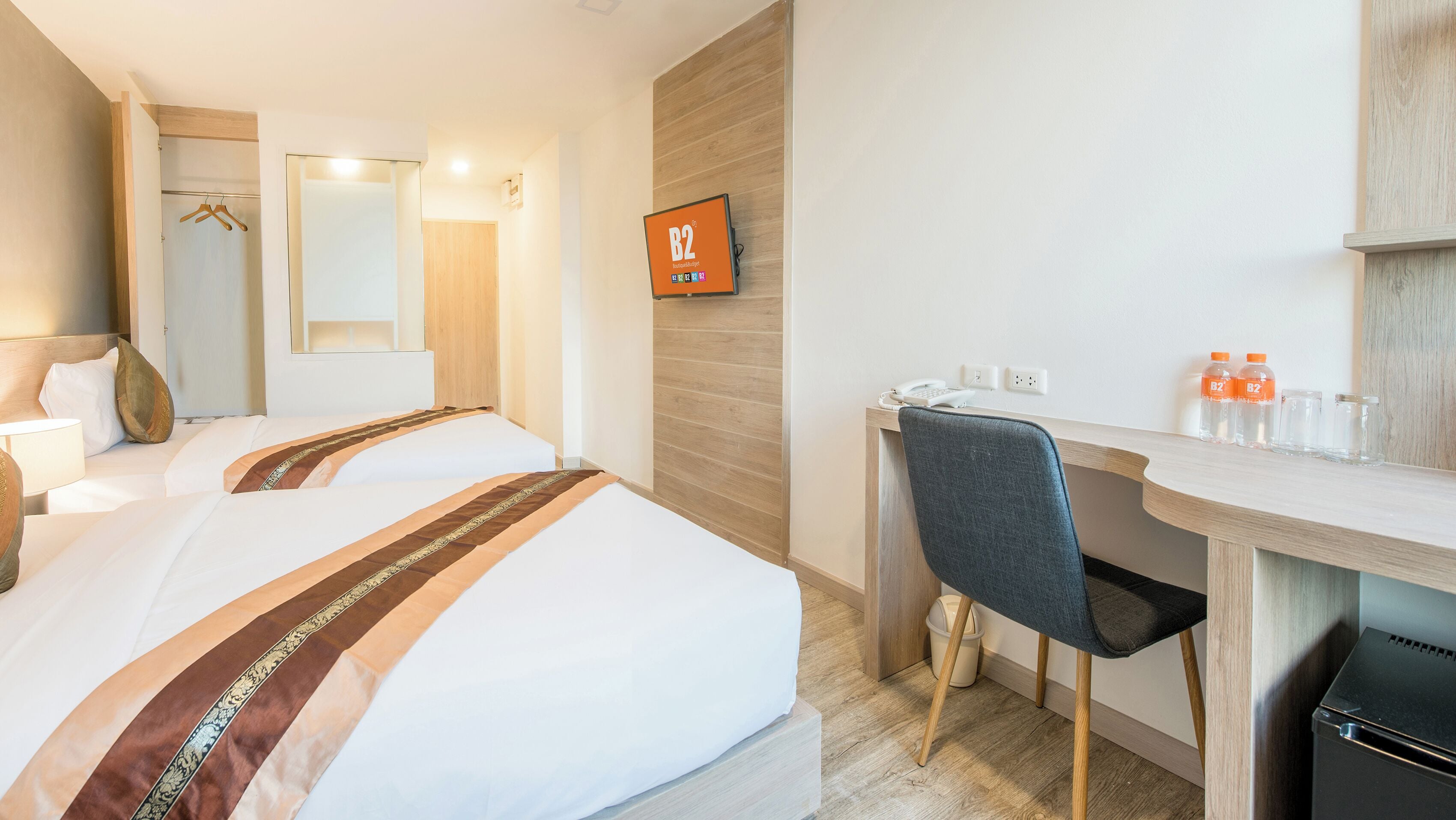 A hotel room with two beds, a desk, a chair, a TV, and a minibar.