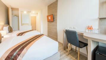 A hotel room with two beds, a desk, a chair, a TV, and a minibar.