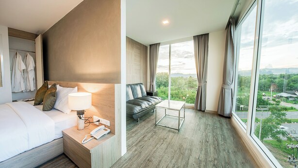 A hotel room with a bed, bedside table with a lamp, a sofa, and a large window offering a city view.
