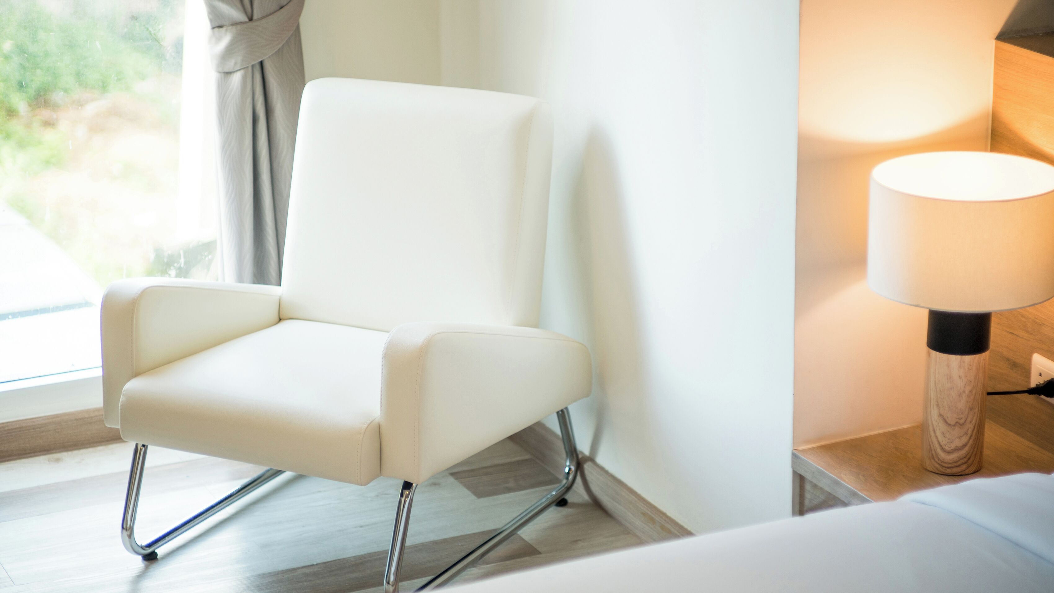 Una silla moderna con patas cromadas, un cojín blanco y una mesita de madera con una lámpara.