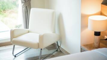 Una silla moderna con patas cromadas, un cojín blanco y una mesita de madera con una lámpara.