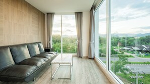 A modern room with a leather sofa, a small table, and a large window offering a view of a green landscape and buildings.