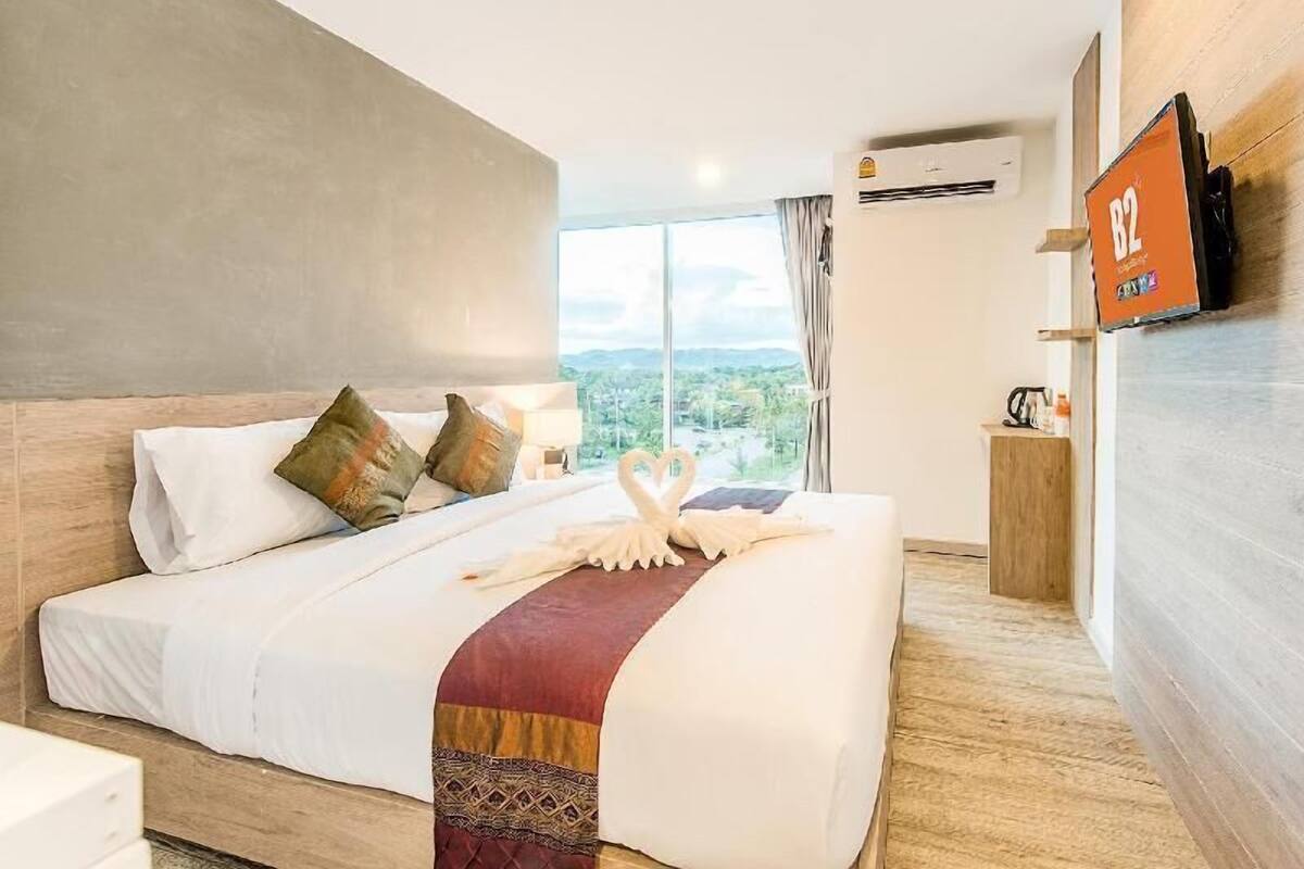 Habitación de hotel con una cama grande, televisión en la pared y vistas al exterior.