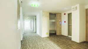 A hotel corridor with a patterned carpet, an elevator, and a door with a red emergency button.