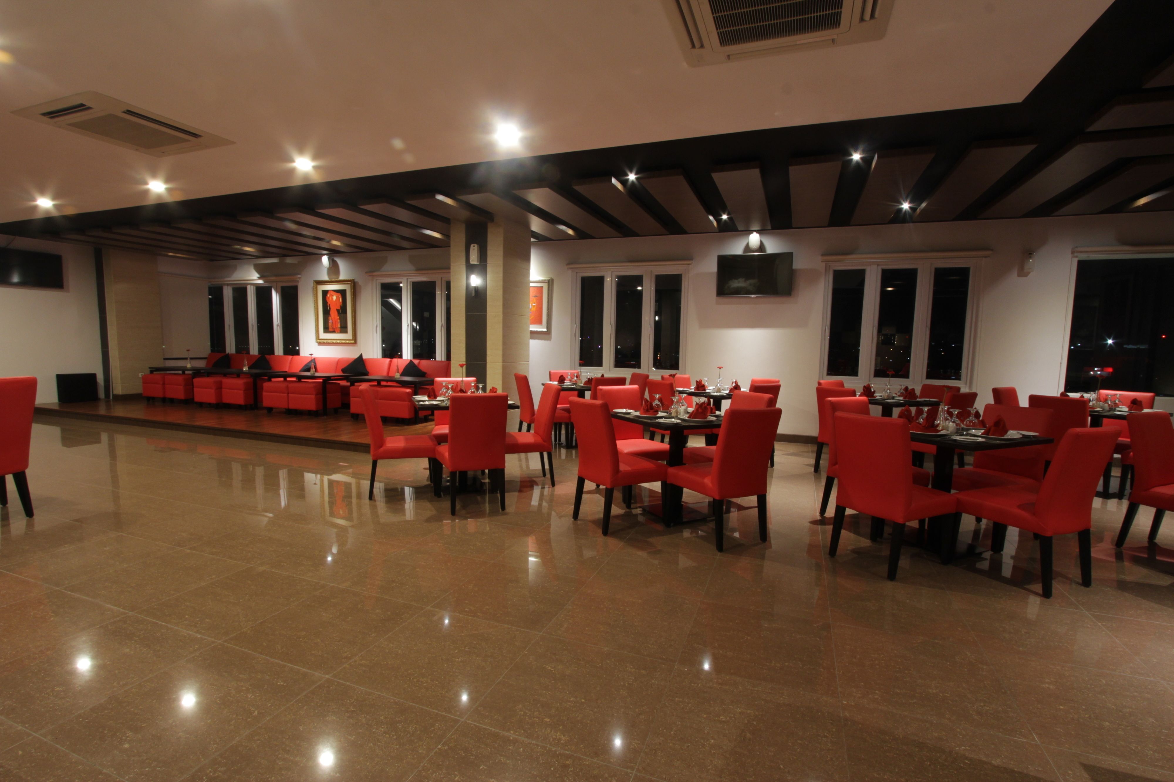 A spacious restaurant with red chairs and tables, large windows, and a modern ceiling design.