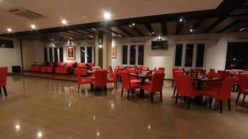 A spacious restaurant with red chairs and tables, large windows, and a modern ceiling design.